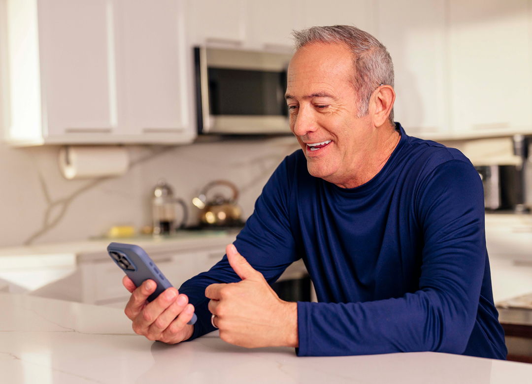 man with silver hair in a blue sweater in a kitchen on a video call